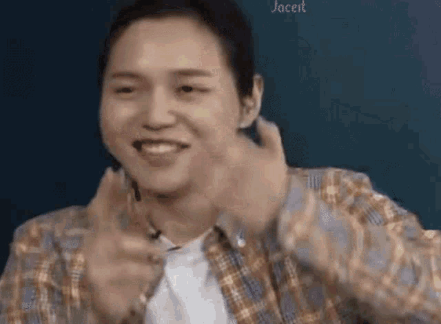 a young man in a plaid shirt is making a funny face while talking on a cell phone .