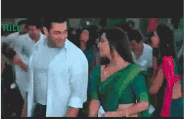 a man in a white shirt and a woman in a green sari are dancing in a crowd with the word ritu in the corner