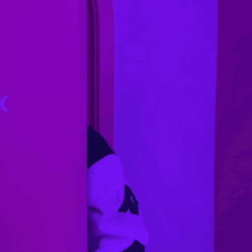 a person peeking out from behind a purple wall with a heart above their head that says ck