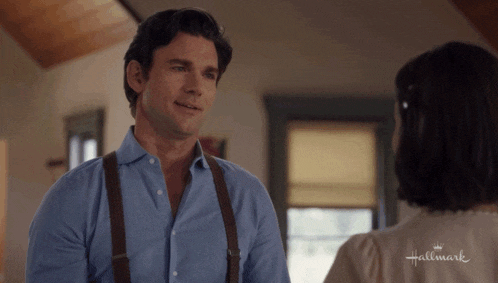 a man in a blue shirt and suspenders is talking to a woman in a hallmark shirt