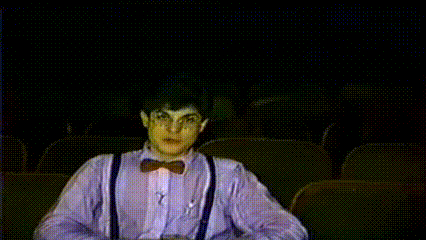 a man wearing suspenders and a bow tie is sitting in a dark auditorium