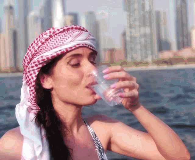 a woman wearing a head scarf is drinking from a clear plastic cup