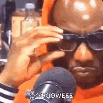 a man wearing sunglasses is sitting in front of a microphone and talking into it .