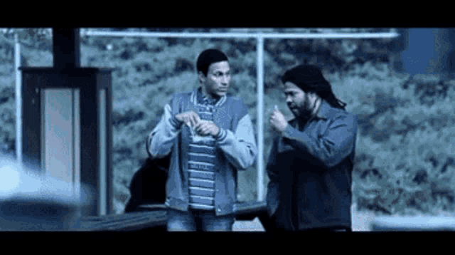 two men are standing next to each other in a dark room talking to each other .