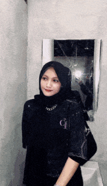 a woman wearing a hijab is taking a selfie in front of a mirror