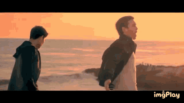 two men are standing on a beach at sunset with a watermark that says imgplay