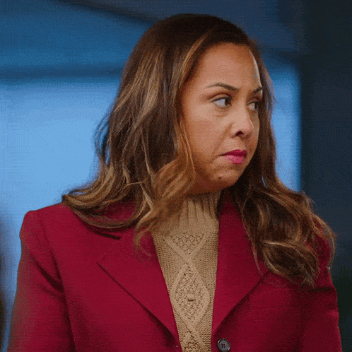 a woman wearing a red jacket and a tan sweater is making a funny face