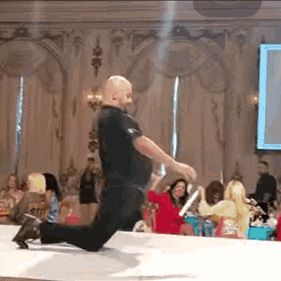 a man is kneeling down on a runway at a fashion show in front of a crowd of people .
