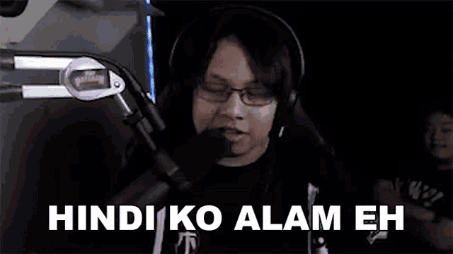 a man wearing headphones and glasses is talking into a microphone and saying `` hindi ko alam eh '' .