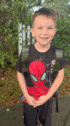 a young boy wearing a spiderman shirt is standing on a sidewalk with his hands folded .