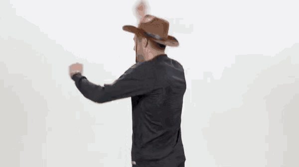 a man wearing a cowboy hat and a black jacket is standing in front of a white wall .
