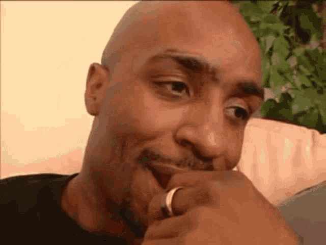 a bald man with a wedding ring on his finger is sitting on a couch with his hand to his mouth .