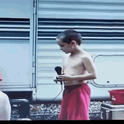 a shirtless young boy in pink shorts is holding a microphone in front of a trailer .