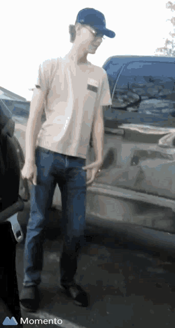 a man wearing a baseball cap and sunglasses is standing in front of a truck .