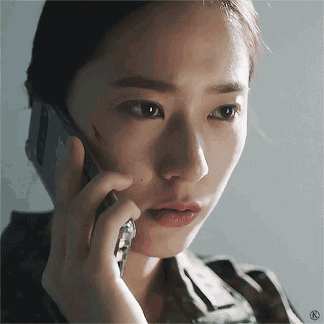 a close up of a woman talking on a cell phone with the letter k on the bottom