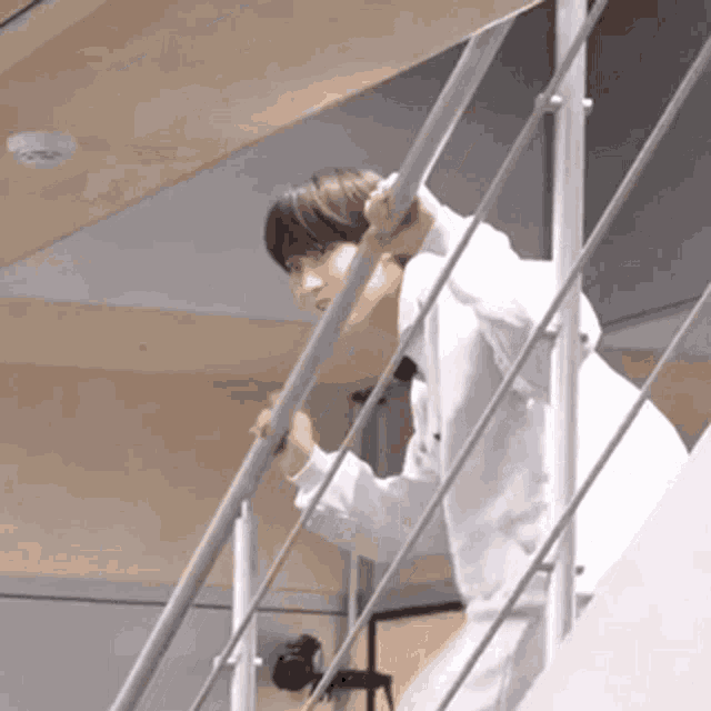 a man in a white coat is standing on a set of stairs holding onto a railing .