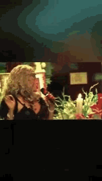 a woman singing into a microphone in front of flowers