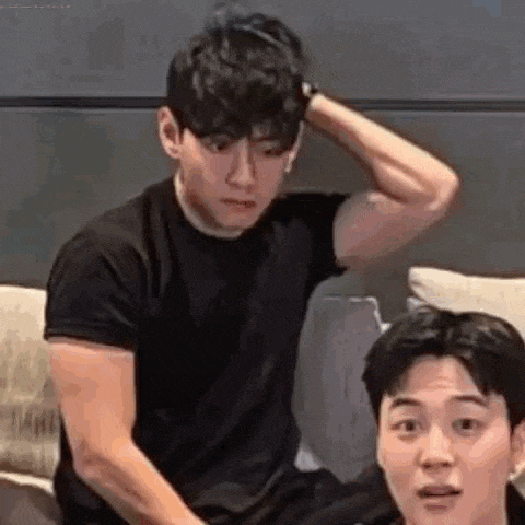 a man is sitting on a couch with his hand on his head and another man is sitting next to him .