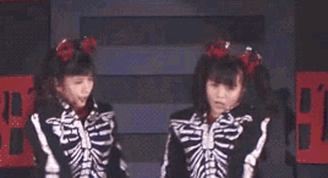 two girls dressed in skeleton costumes are standing next to each other on a stage .