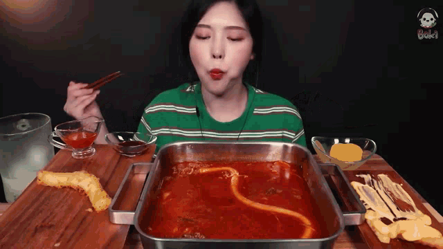 a woman in a green and red striped shirt is eating a pot of sauce