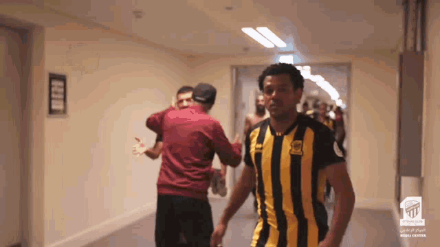 a man in a yellow and black striped shirt is walking down the hallway
