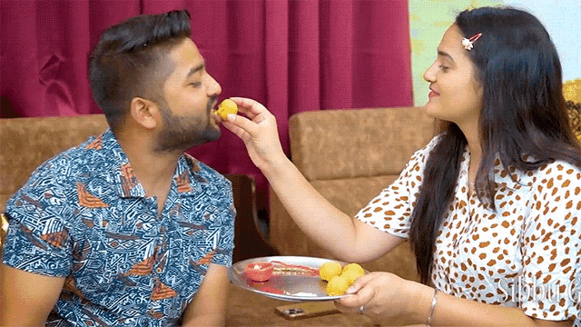 a woman feeding a man a piece of food from a plate