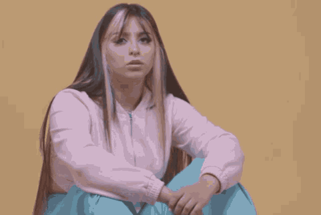 a woman in a pink jacket and blue pants sits on the floor