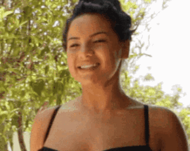 a woman in a black bra is smiling with trees in the background