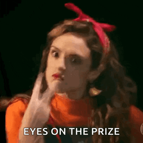 a woman wearing a red headband and an orange sweater is holding her hand to her chin and says eyes on the prize .