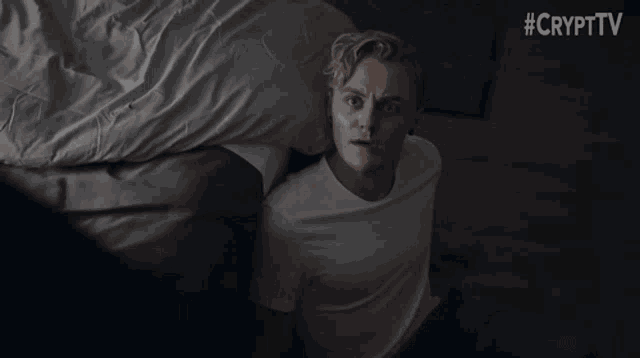 a man in a white t-shirt is laying on a bed with #crypttv written on the bottom