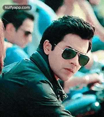 a man wearing sunglasses is sitting on a motorcycle in a crowd .