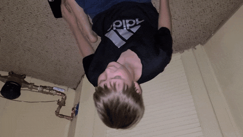 a boy is upside down wearing a black adidas shirt