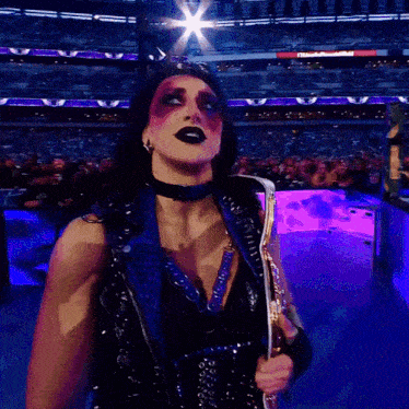 a female wrestler is holding a trophy in front of a crowd that is watching a wrestling match