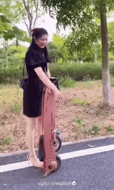a woman in a black dress is pushing a skateboard on the side of the road ..