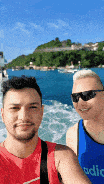 two men posing for a picture with one wearing a blue tank top that says adidas