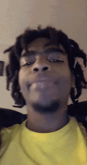 a man with dreadlocks is wearing a yellow shirt and making a face