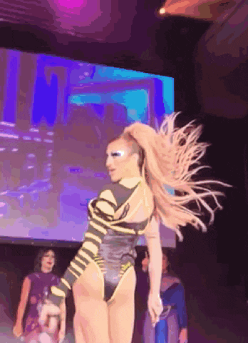 a drag queen is dancing on a stage in front of a screen