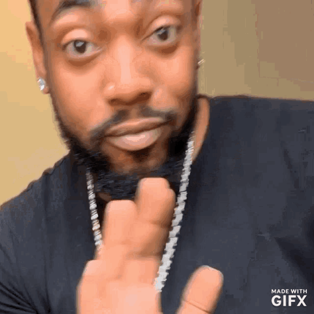 a man with a beard is wearing a black shirt and a chain around his neck