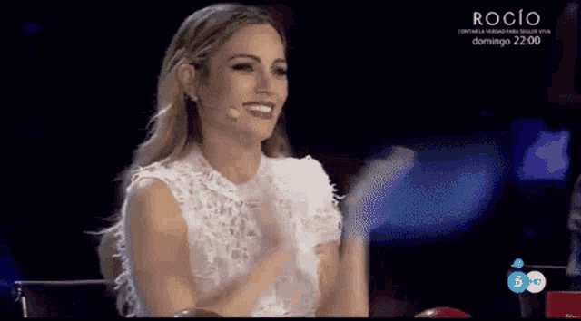 a woman in a white dress is sitting in front of a microphone and applauding