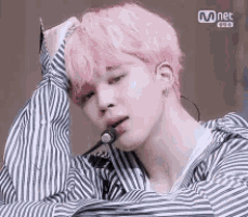 a man with pink hair is wearing a striped shirt and a microphone .