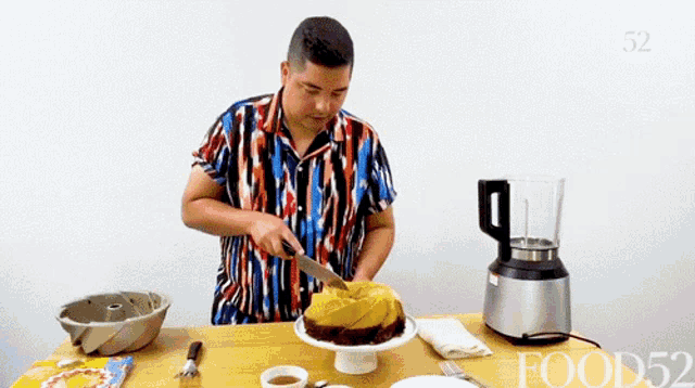 a man is cutting a cake with a knife in front of a blender that says food52
