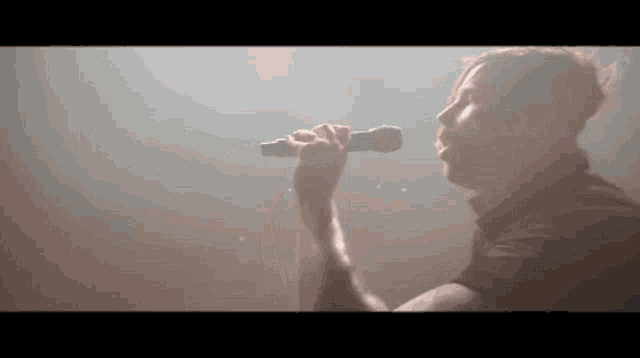 a man in a black shirt is singing into a microphone in a dark room