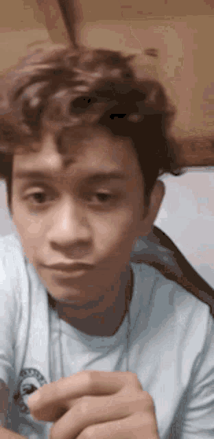 a young man with curly hair is making a funny face while wearing a light blue shirt .