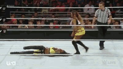 a woman is laying on the ground in a wrestling ring while a referee walks around .