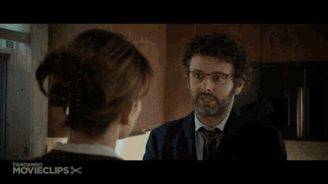 a man in a suit and tie talks to a woman in a kitchen in a movie clip