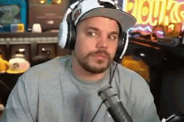 a man wearing headphones and a hat is sitting in front of a microphone and looking at the camera .