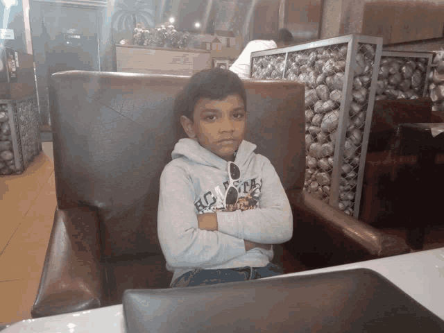 a young boy sits in a chair with his arms crossed wearing a sweatshirt that says hospitals