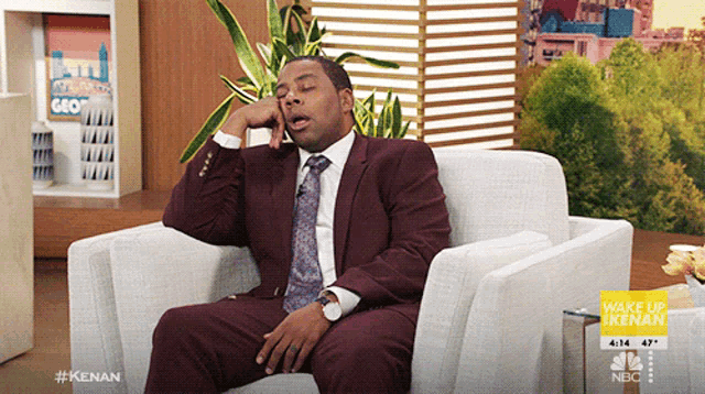 a man in a suit and tie is sitting in a chair talking on a phone