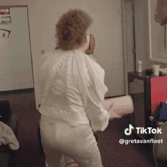 a woman in a white shirt and white pants is dancing in a room with a tiktok watermark