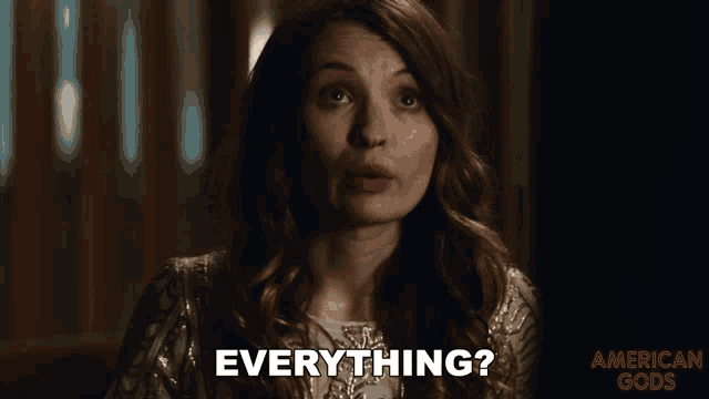 a woman says " everything " in front of an american gods ad